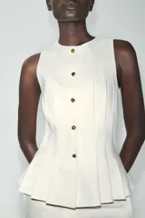 Chaleco entallado blanco con cuello redondo, manga sisa, pinzas estructuradas, detalle de peplum en la parte inferior y cierre frontal con botones dorados.