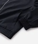 Campera masculina de corte boxy en color beige, con cuello inglés, cierre frontal de cremallera, mangas largas con puños elásticos y ruedo con elástico. Presenta bolsillos laterales y detalles de recortes en el diseño.