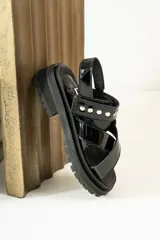Sandalias de cuero marrón con textura de cocodrilo, diseño de tiras cruzadas con tachas metálicas plateadas y suela track negra de plataforma.