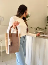 Bolso matero de cuero color taupe con textura croco y detalles en cuero color marrón. Tiene doble asa de mano y un dije de borla.
