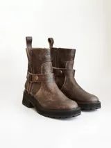 Bota corta de cuero vacuno en color chocolate con efecto desgastado. Presenta una suela track de goma negra, detalle de pulsera desmontable con tachas metálicas y cierre lateral.