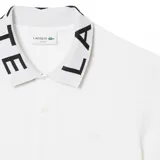 Remera polo de manga corta Lacoste, color blanco, confeccionada en tejido piqué con cuello clásico que presenta inscripciones de la marca en contraste.