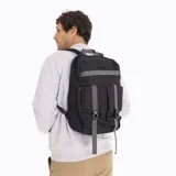 Mochila urbana Merrell de color negro con detalles en gris. Cuenta con un compartimento principal con cierre, un bolsillo frontal con solapa y correas ajustables con hebillas de plástico. Presenta una cinta horizontal decorativa y el logo de la marca en la parte superior.