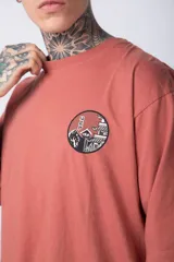 Remera de corte oversize color terracota, con cuello redondo y manga corta. Presenta un estampado circular pequeño en el pecho con motivos orientales.