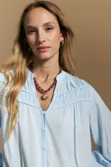 Camisa de manga larga color blanco, con cuello mao y escote en V. Presenta frunces en el canesú, cierre frontal con botones y mangas amplias con puños abotonados.