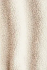 Campera oversized de sherpa suave color beige, con cuello elevado, cierre frontal y bolsillos discretos en las costuras laterales. Presenta hombros caídos y mangas largas amplias.