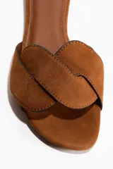 Sandalias planas de gamuza color marrón tostado, con punta almendrada y una tira ancha trenzada en el empeine. Cuentan con plantilla de cuero y bordes ribeteados en color negro.