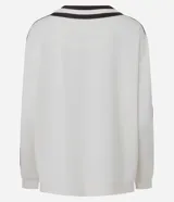Cardigan deportivo de corte oversized, color blanco con detalles en marrón oscuro. Presenta escote en V, cierre frontal con botones a presión, mangas largas con franjas laterales y puños acanalados. Incluye un parche circular con letras en el pecho.