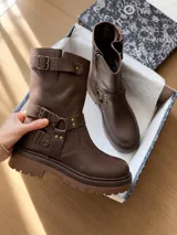 Bota de caña media confeccionada en cuero, con diseño de hebillas laterales decorativas y suela track resistente.