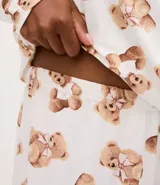 Pijama largo de dos piezas compuesto por una blusa de manga larga con escote redondo y un pantalón con cintura elástica. Presenta un estampado integral de ositos sobre un fondo blanco.