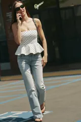 Top palabra de honor de color blanco con estampado de lunares negros, diseño sin tirantes y bajo con volados tipo peplum.