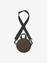 Cartera circular de Carhartt en color marrón, con logo grabado en relieve en el frente. Cuenta con una manija superior pequeña, cierre perimetral y una correa larga ajustable y extraíble en color negro.