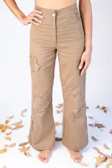 Pantalón largo color beige con parches en forma de flor con bordes desflecados.