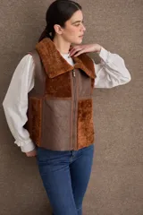 Chaleco de cuero y piel sintética en color marrón, con diseño de paneles combinados, cuello solapa y cierre frontal con cremallera.