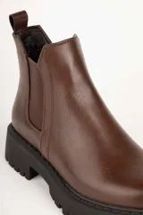 Bota estilo Chelsea de caña baja confeccionada en cuero sintético, con punta redonda, paneles elásticos laterales y suela track dentada de plataforma.