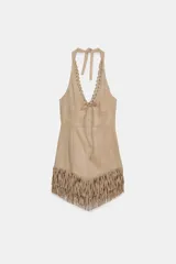 Vestido corto de estilo western con cuello halter y escote en pico con lazada frontal. Presenta un diseño ajustado en el torso y un bajo asimétrico decorado con flecos largos.