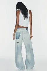 Jeans de tiro medio y corte baggy con cinco bolsillos, trabillas y rotos decorativos. Cuenta con detalle de cinturón confeccionado en el mismo tejido y cierre frontal con cremallera y botón metálico.
