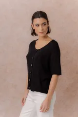 Cardigan tejido de manga corta color beige, con escote redondo amplio y abotonadura frontal con botones al tono. Presenta un calce relajado y terminaciones en rib en la cartera y el ruedo.