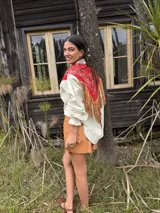 Camisa de jean color crudo con canesú rojo con estampado paisley y flecos de cuero marrón en la espalda. Cuenta con cuello camisero, mangas largas con puños fruncidos y cierre frontal con botones.