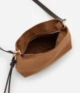 Bolso bandolera de tamaño mediano confeccionado en gamuza sintética color marrón tostado. Presenta un formato rectangular estructurado, cierre superior con cremallera y correa larga ajustable en color marrón oscuro. Incluye un detalle decorativo de tiras anudadas en uno de los laterales.