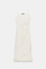 Vestido midi lencero de color blanco, confeccionado en tejido con efecto arrugado. Cuenta con escote recto, tirantes finos ajustables, diseño cruzado con cinturón fino para anudar y detalles de encaje en los acabados de la falda.