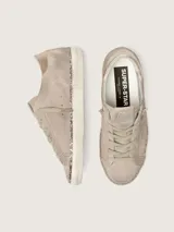 Zapatillas Golden Goose modelo Super-Star en gamuza color topo. Presentan diseño de aspecto desgastado, con la clásica estrella lateral en el mismo tono, contrafuerte metalizado en color bronce, cordones tono sobre tono y detalle de glitter champagne en el canto de la suela.