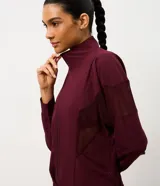 Campera deportiva tipo rompevientos color bordó, con cierre frontal, cuello alto y mangas largas. Presenta paneles laterales de tul para mayor ventilación y cordón ajustable en la cintura.