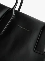 Cartera tote negra Tommy Hilfiger de acabado liso, con dos asas superiores y cierre de cremallera. Incluye un compartimento principal, un bolsillo interior con cremallera y logo metálico en relieve en la parte delantera.