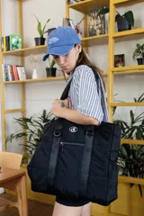 Bolso tipo tote de diseño urbano, confeccionado en material impermeable acolchado de color negro. Cuenta con doble asa de hombro, compartimento principal con cierre, bolsillo frontal con cierre y detalle de logo circular en la parte superior.