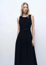 Vestido midi negro sin mangas, con cuello redondo, cinturón con hebilla y falda evasé con pliegues. Presenta cierre lateral con cremallera y botón en la parte posterior.