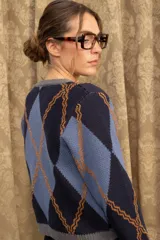 Cardigan de punto con patrón argyle en tonos azul marino, celeste y naranja. Presenta cuello redondo, cierre frontal con botones dorados y terminaciones en tejido acanalado gris.