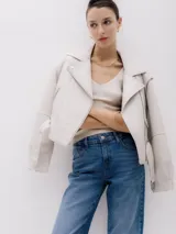Chaqueta corta estilo biker color beige, confeccionada en piel sintética. Presenta cierre asimétrico frontal, bolsillo con cierre a la vista y bolsillo con solapa, cinturón con hebilla en la cintura.