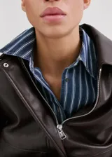 Camisa oversize de algodón estilo denim, de color azul con estampado de rayas, cuello camisero, manga larga con puños abotonados, bolsillo de parche en el pecho y cierre frontal con botones.