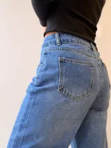 Pantalón de jean corte mom fit con tiro alto, confeccionado en denim de lavado clásico. Presenta cierre frontal con botón y cierre metálico, con bolsillos funcionales delanteros y traseros.