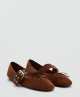 Zapatos planos de gamuza marrón, con punta fina, cierre de dos tiras con hebillas metálicas en el empeine y detalle de lazo pequeño en la puntera.
