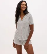 Pijama tipo short doll de viscolycra, compuesto por una camisa de manga corta con cuello solapa y cierre frontal de botones, y un short con cintura elástica. Presenta un estampado de rayas verticales con pequeños moños distribuidos por toda la prenda.
