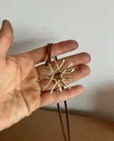 Collar artesanal con dije de diseño orgánico en metal y tiento de gamuza ajustable. El dije presenta una forma circular con terminaciones curvas, evocando un diseño natural.