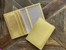 Tarjetero de cuero vacuno color dorado con ranuras para tarjetas y bolsillo exterior en la parte trasera.