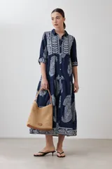 Maxi vestido azul marino con estampado de arabescos en blanco, corte camisero, cuello clásico, mangas 3/4 y falda escalonada.