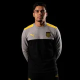 Buzo de cuello redondo Puma, parte de la indumentaria oficial del Club Atlético Peñarol. Presenta un diseño de bloques de color, con la parte superior en gris, hombros en amarillo y la parte inferior en negro. Incluye el logo de Puma en amarillo en el pecho derecho y el escudo del club en el pecho izquierdo.