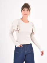 Remera de manga larga en color beige, confeccionada en tejido acanalado, con cuello redondo y detalle de volados en los hombros.