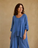 Blusa azul jean de corte asimétrico y holgado, con cuello redondo, mangas largas con detalle de presilla para arremangar y aplique de tejido calado en el bajo.