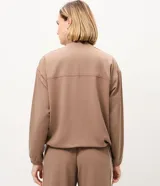 Campera deportiva oversized de microfibra color marrón, con cuello alto, cierre frontal y bolsillos laterales. Presenta bandas laterales contrastantes en las mangas y cordón ajustable en el dobladillo.