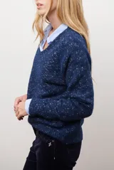 Buzo de punto color gris claro con motas oscuras, escote en V y mangas largas.