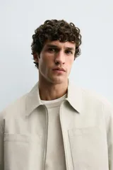 Sobrecamisa de corte regular confeccionada en tejido con estructura canvas color marrón. Presenta un ligero acolchado interior, cuello de solapa y cierre frontal con cremallera metálica. Incluye dos bolsillos de plastrón en el pecho y bolsillos laterales de vivo, con mangas largas terminadas en puños con botón.