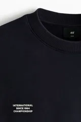 Buzo negro de algodón con diseño estampado en el pecho que incluye texto pequeño y el número '94 en celeste, corte holgado y hombros caídos.