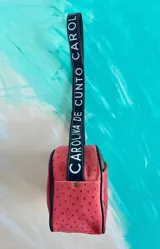 Bandolera Kaira de la línea Ottenta de Carolina De Cunto, en color fucsia metalizado. Cuenta con un diseño compacto, bolsillo exterior con broche imantado y detalle pintado a mano, cierre superior y una correa larga regulable con el logo de la marca estampado.