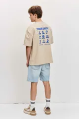 Remera de corte oversize color blanco tiza, de manga corta y cuello redondo, con pequeño estampado gráfico azul en el pecho.