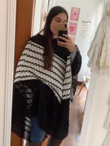 Poncho de tejido abierto en color negro con una franja diagonal en color blanco, con patrón geométrico texturizado.