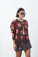 Cardigan de tejido jacquard color marrón con estampado floral en tonos rojo y rosado. Presenta cuello redondo, cierre frontal con botones y terminaciones acanaladas en puños y ruedo.